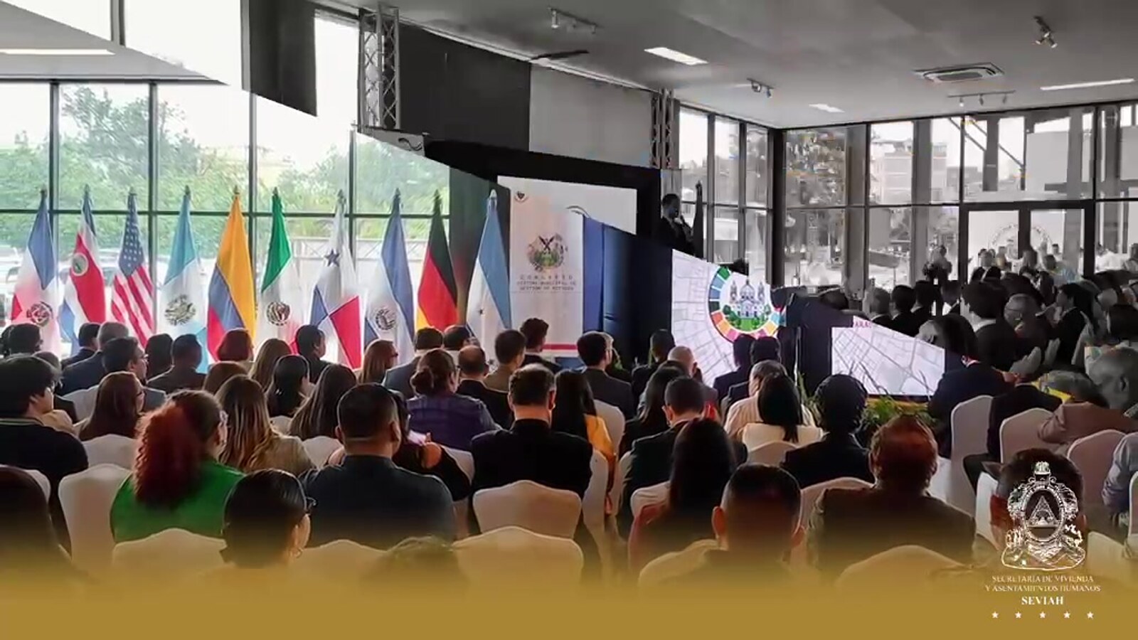 Auditorio del Congreso Municipal Sobre Gestión de Riesgos, con las banderas de los países participantes y el público siguiendo la ponencia